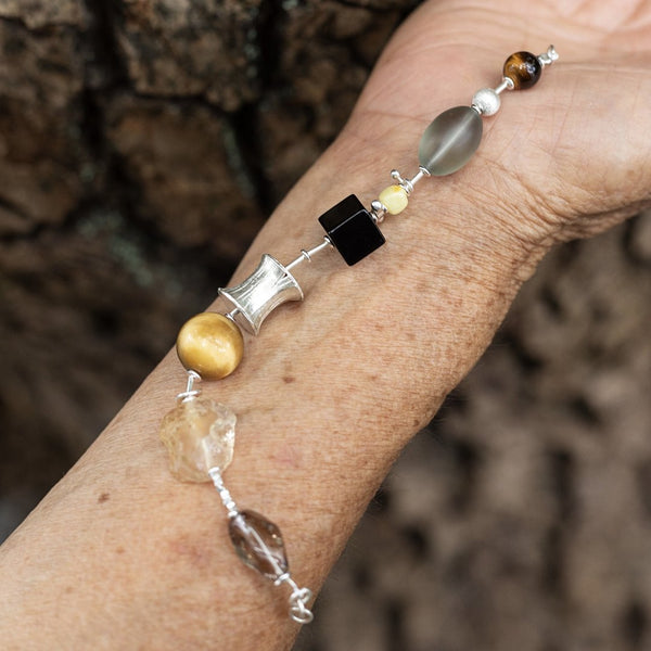 Five Colours of Earth, handmade citrine, tiger's eye and smoky quartz bracelet worn on the hand against tree bark