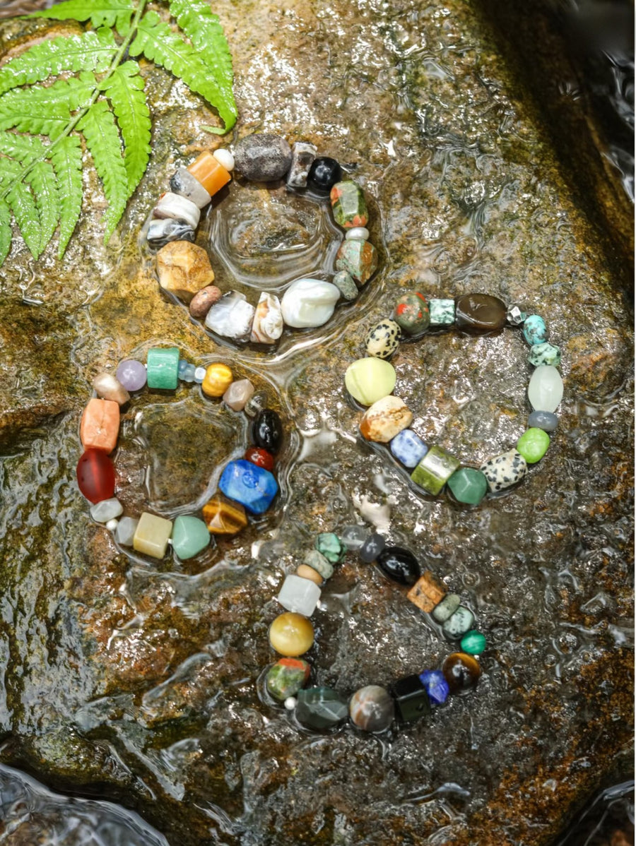 Four chunky stone bracelets resting in a shallow creek beside a fern
