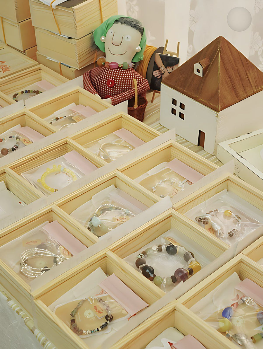 Rows of open wooden boxes, each holding a bracelet on a pink card, ready to ship