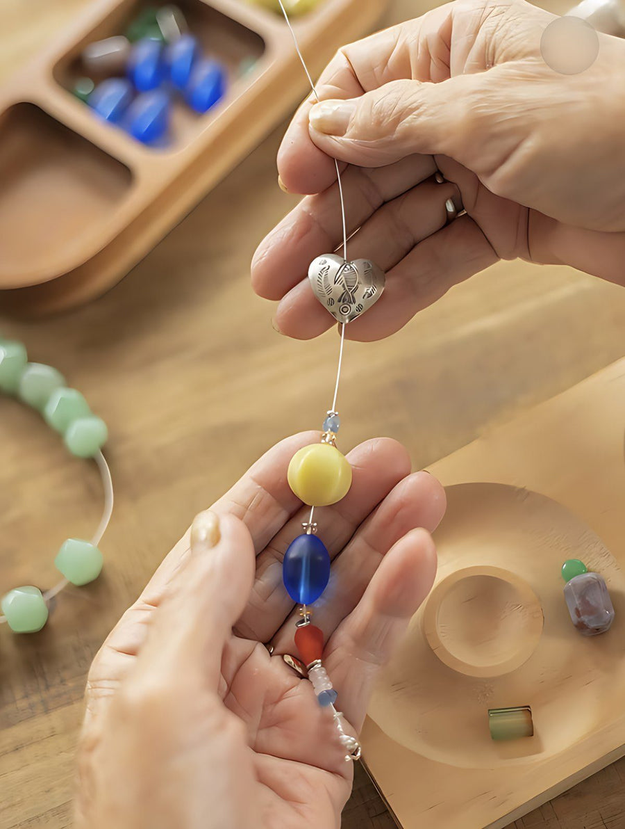 Grandma threading a silver heart charm and blue glass bead onto wire
